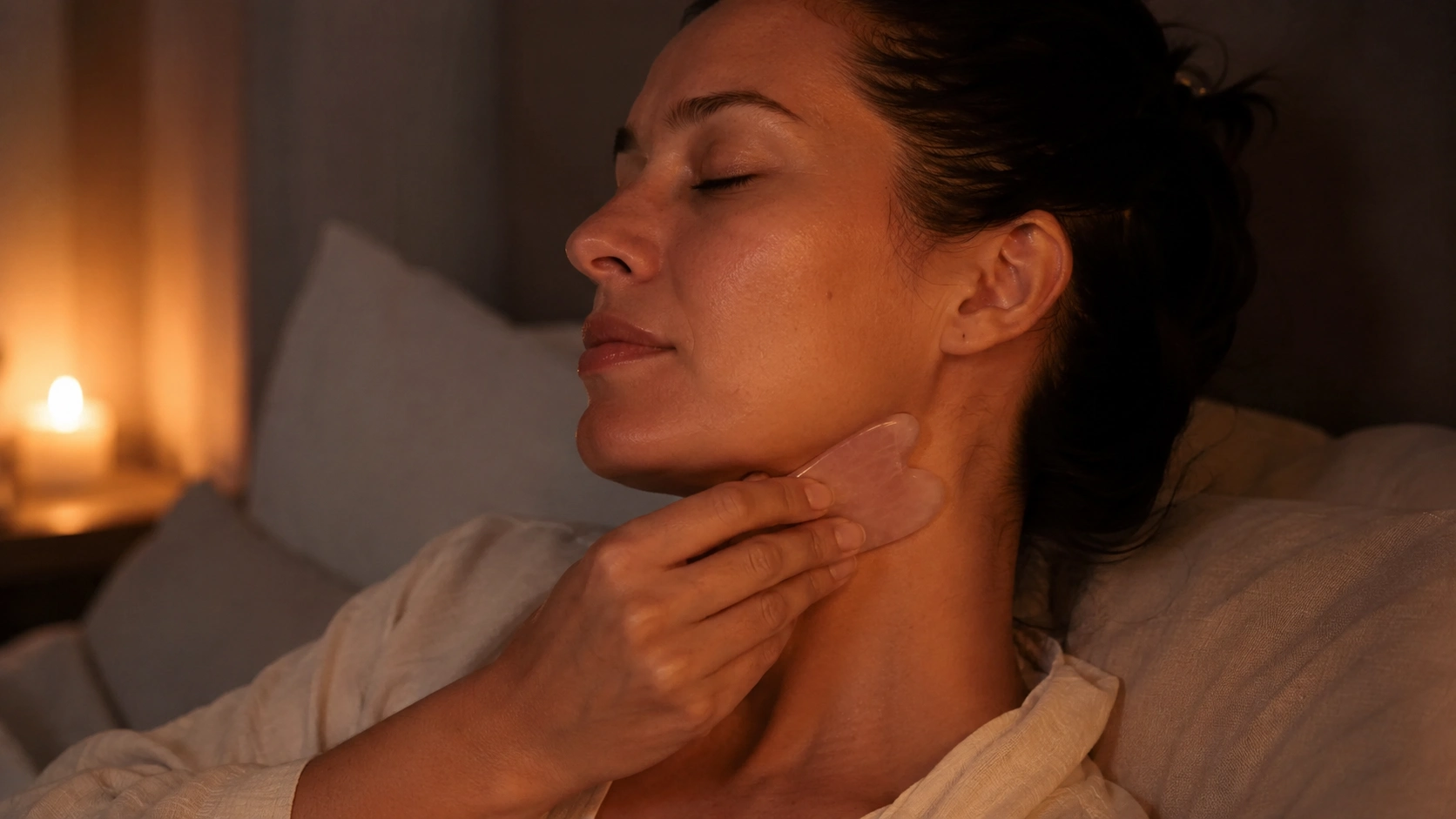 woman uses a rose quartz gua sha tool along her jawline during a calm nighttime skincare routine in bed session