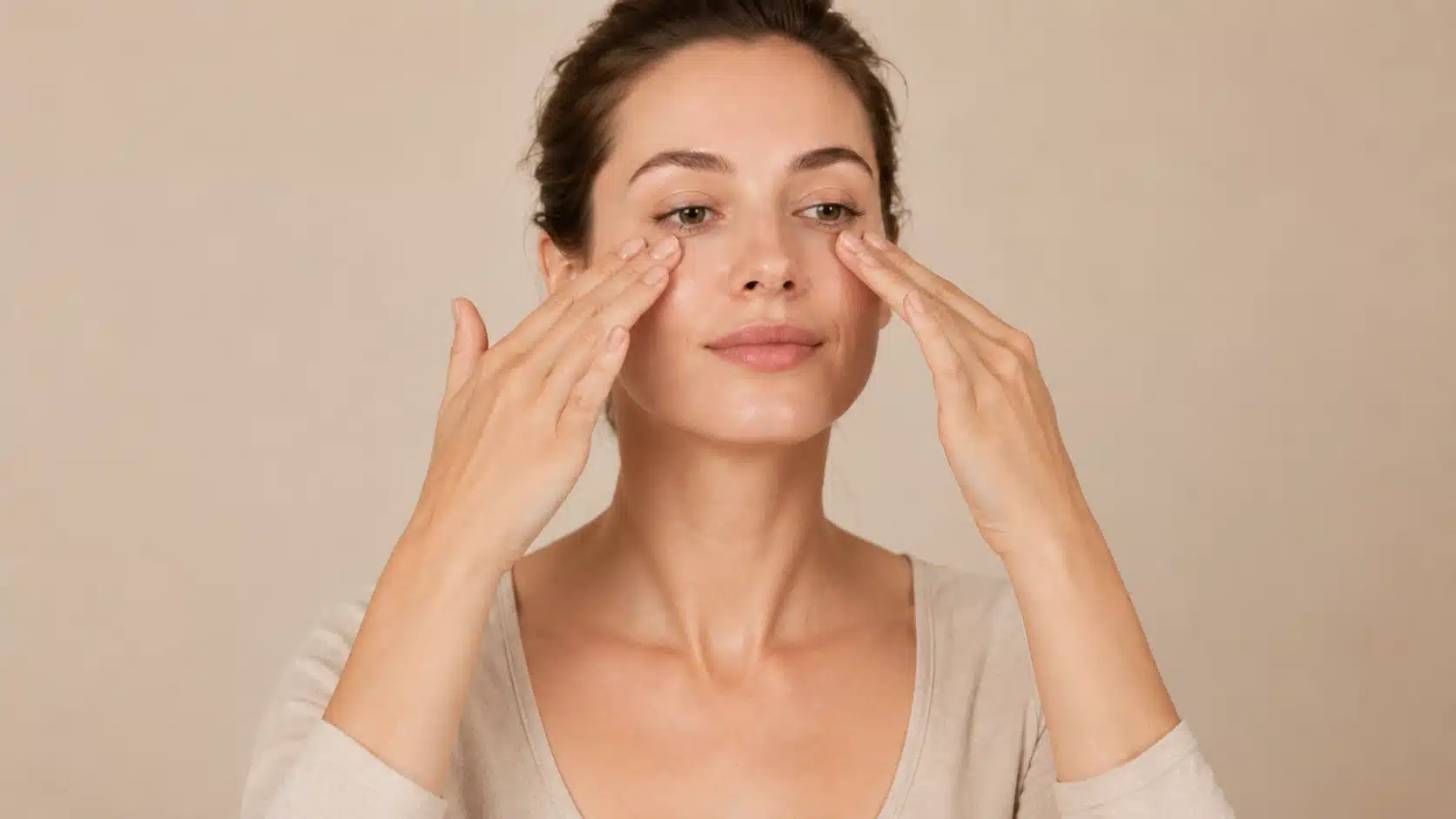 woman using ring fingers under eyes for gentle outward facial massage in soft lighting setting