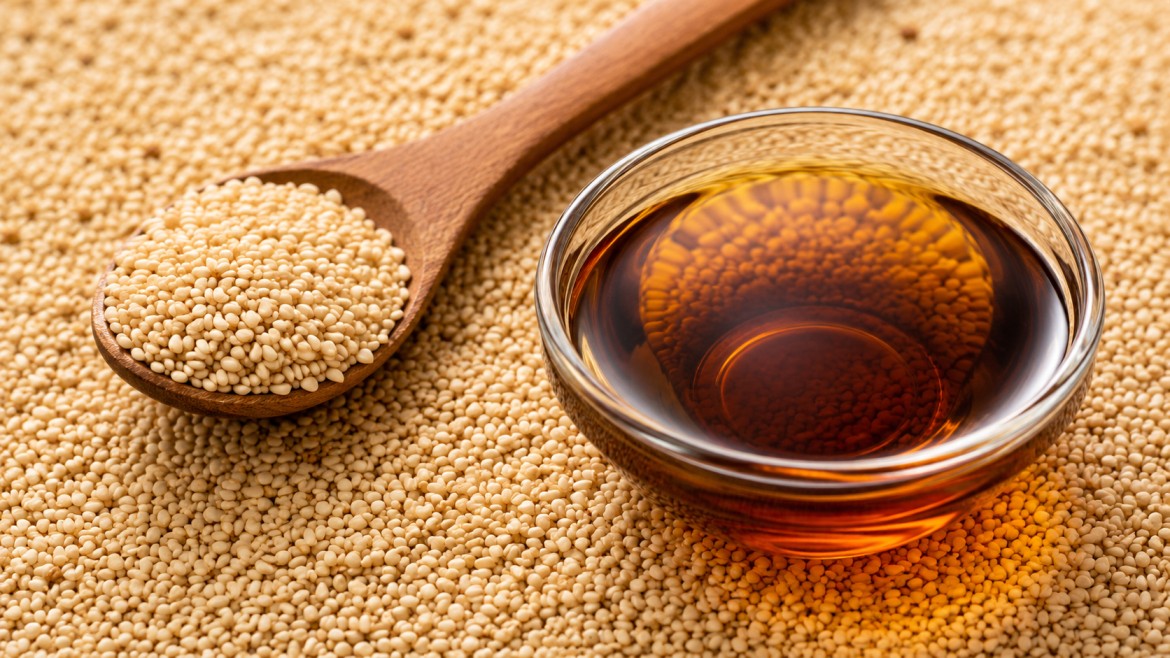 Wooden spoon with sesame granules and a glass bowl of sesame oil on a bed of granules