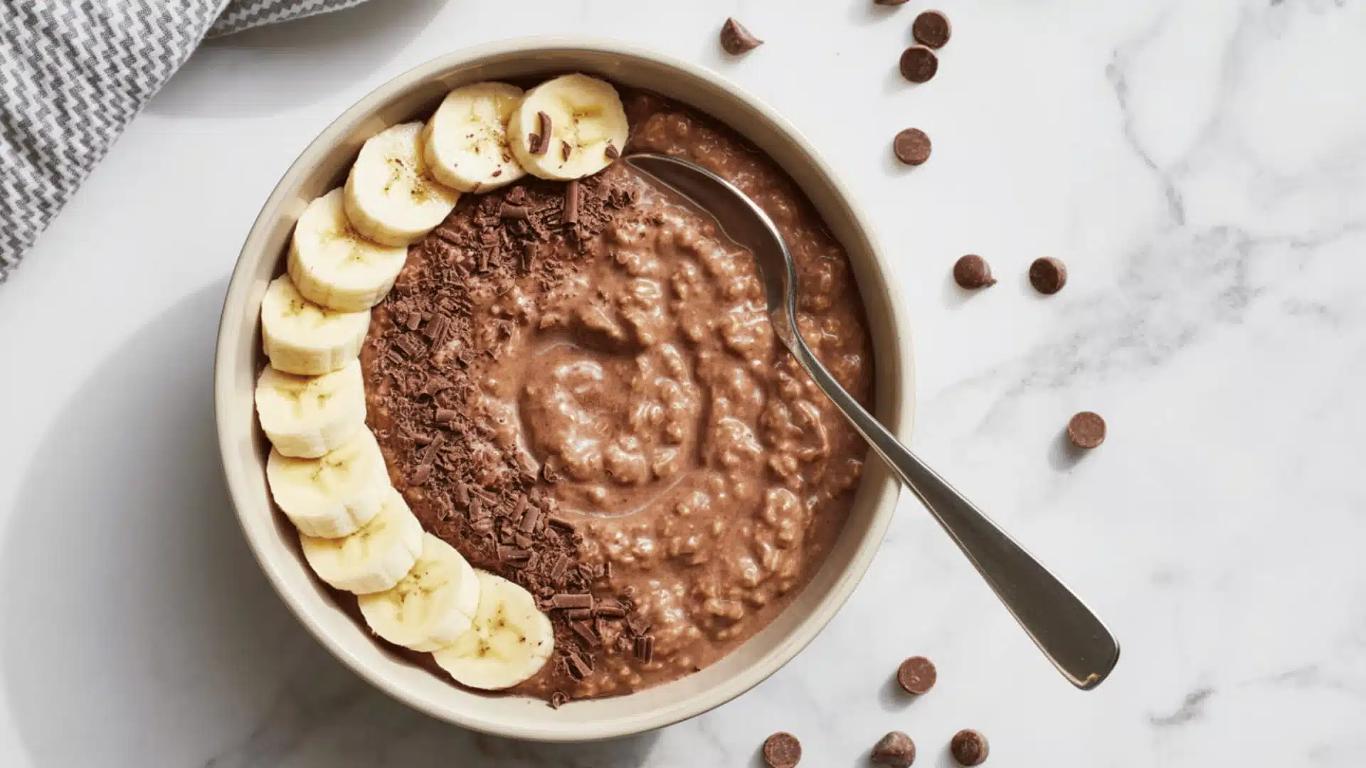 bowl on a white marble surface the bowl contains creamy chocolate-colored oatmeal topped with fresh banana slices