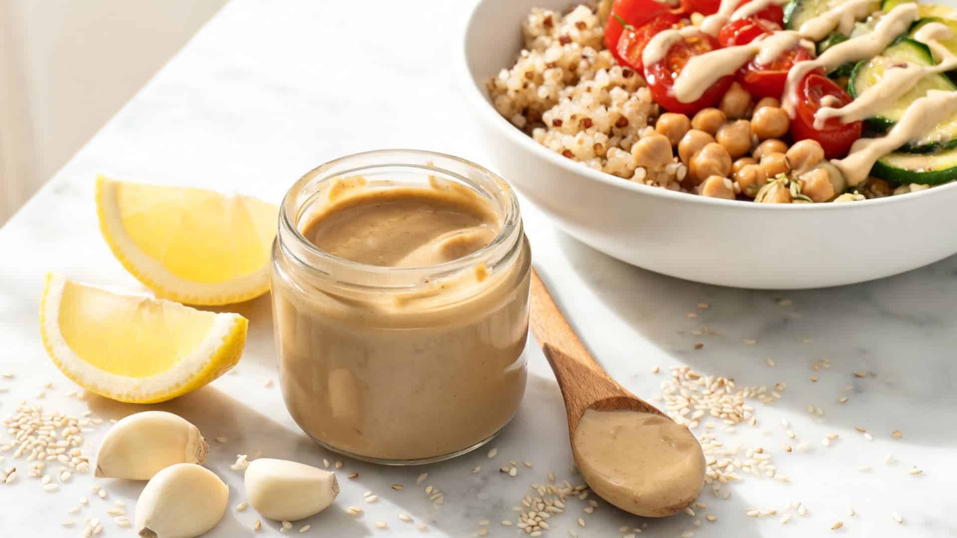 creamy tahini dressing with lemon garlic sesame seeds and a quinoa chickpea veggie bowl in the background