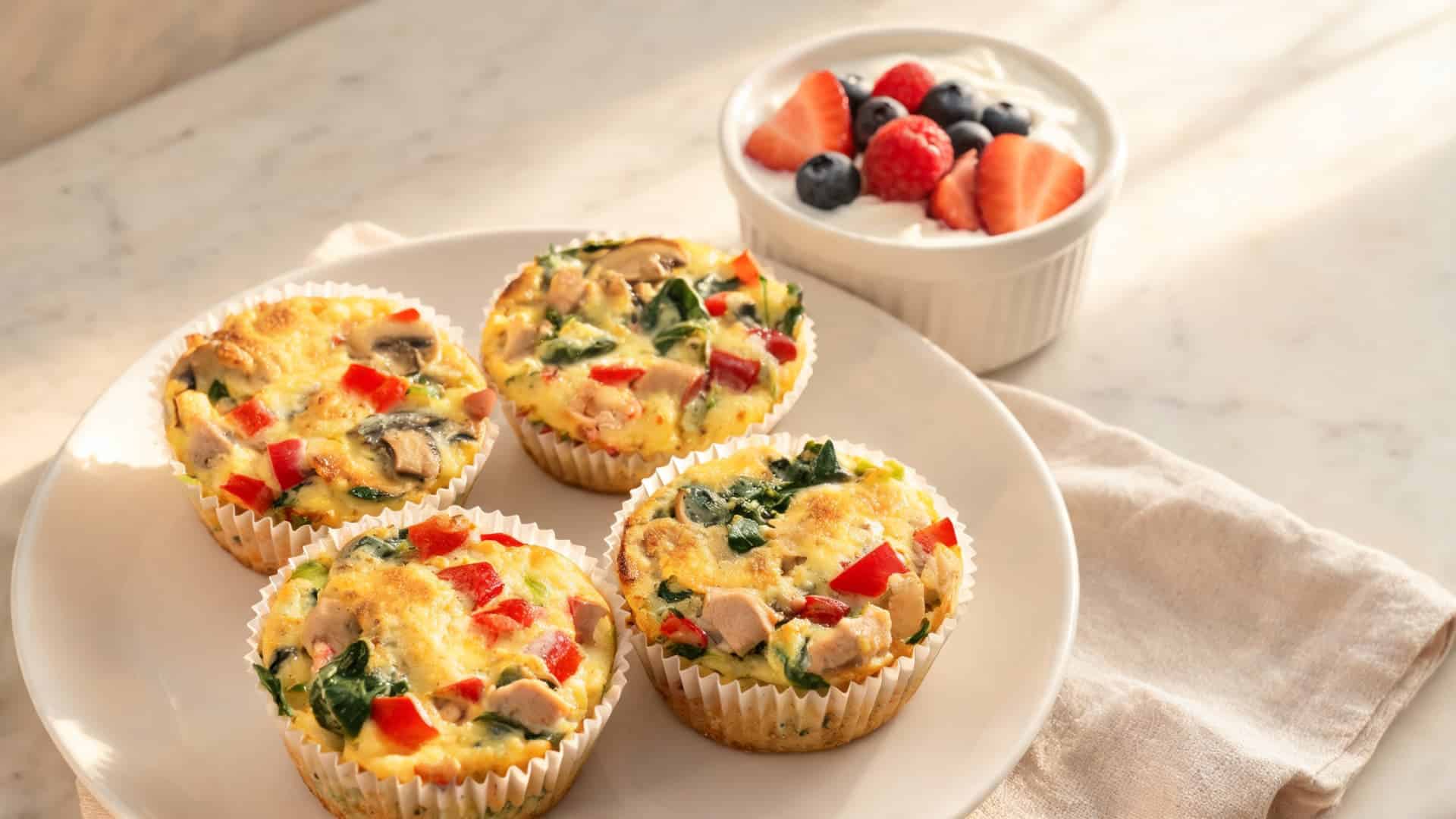egg muffins with spinach, mushrooms, peppers and cheese served with a small bowl of yogurt and berries
