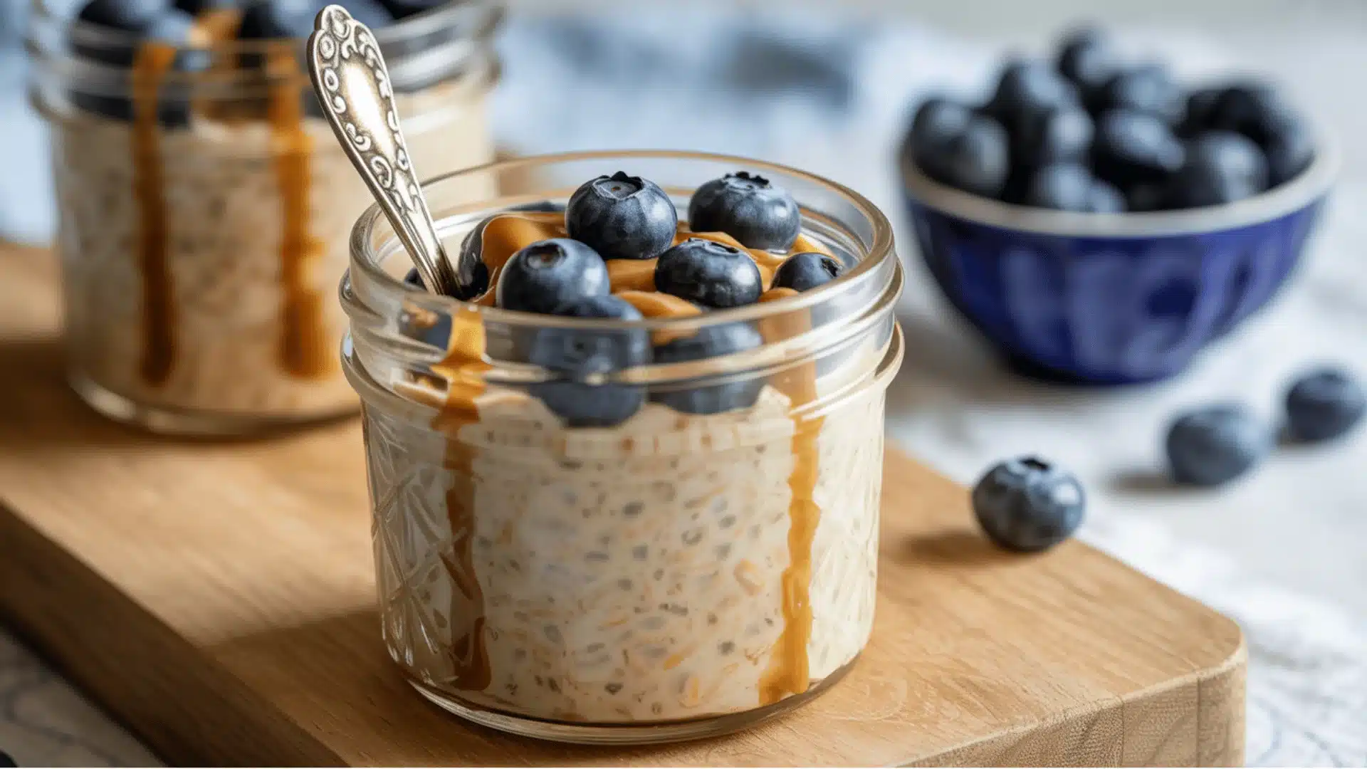 overnight oats in a glass mason jar the oats are topped with fresh, plump dark blue blueberries and drizzled with caramel sauce