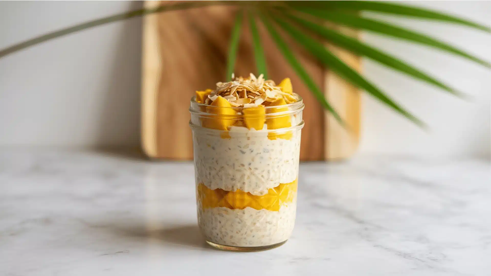 _photograph of overnight oats in a clear glass mason jar on a white marble surface oats are layered with bright yellow mango chunks  (1)