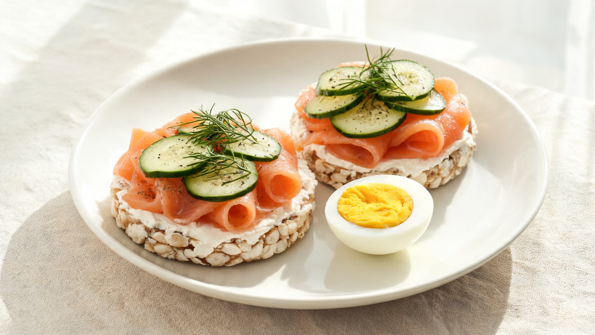 rice cakes with cream cheese, smoked salmon, cucumber, dill and a boiled egg on a white plate