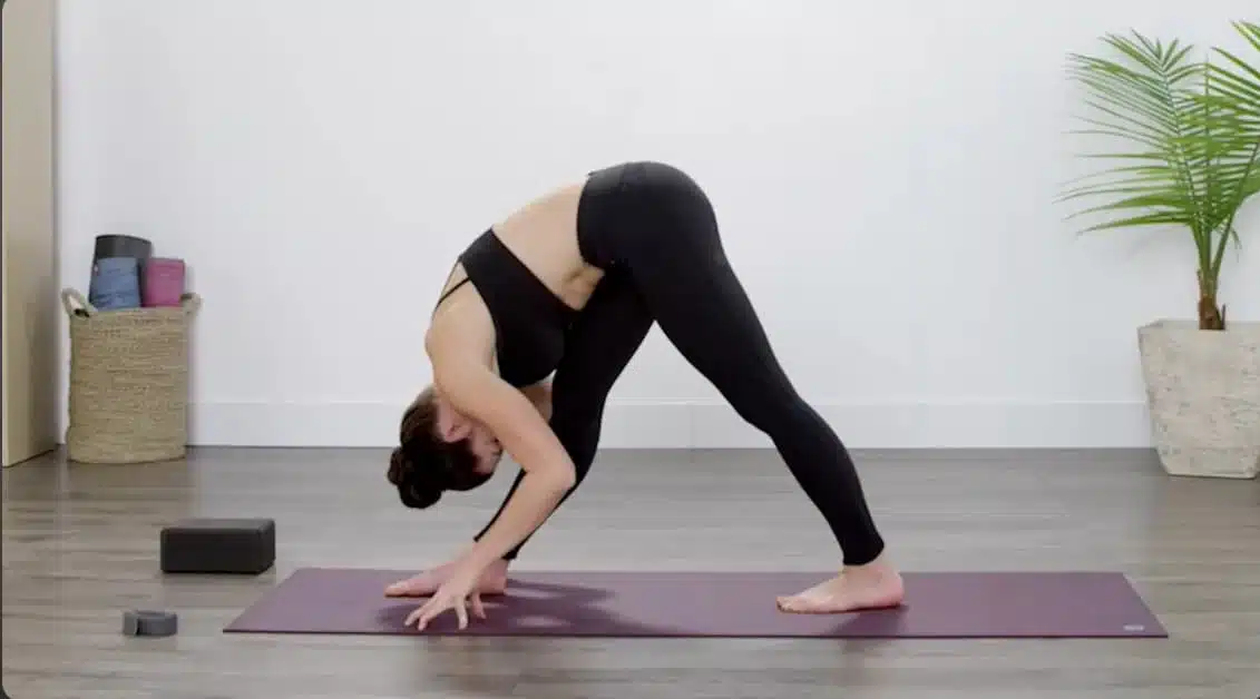 woman holding pyramid pose with one hand near the foot and the spine softly rounded