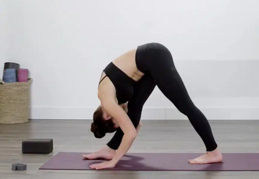 woman in pyramid pose with both hands grounded and legs active on a purple yoga mat