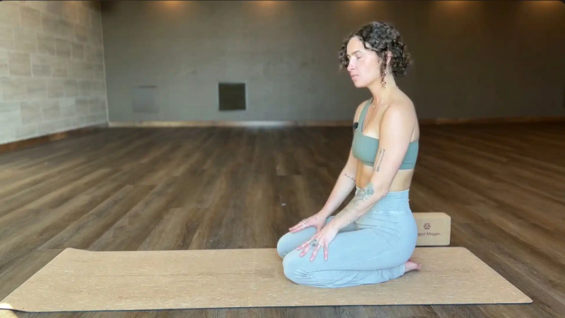 woman kneeling on a yoga mat in a calm studio preparing to begin puppy pose