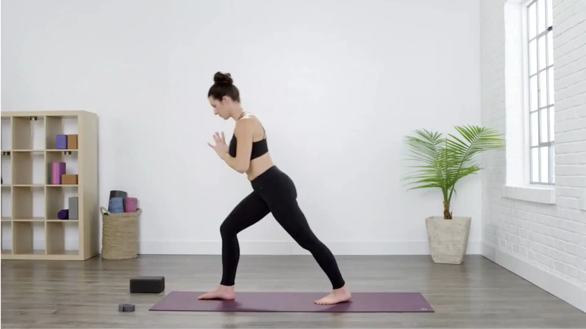 woman setting up pyramid pose in a bright yoga studio with palms together and a steady stance