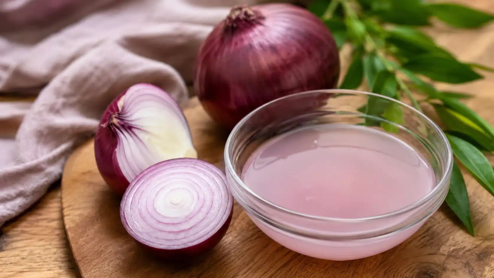 glass bowl of fresh onion juice with sliced and whole red onions on a wooden surface for natural hair care section