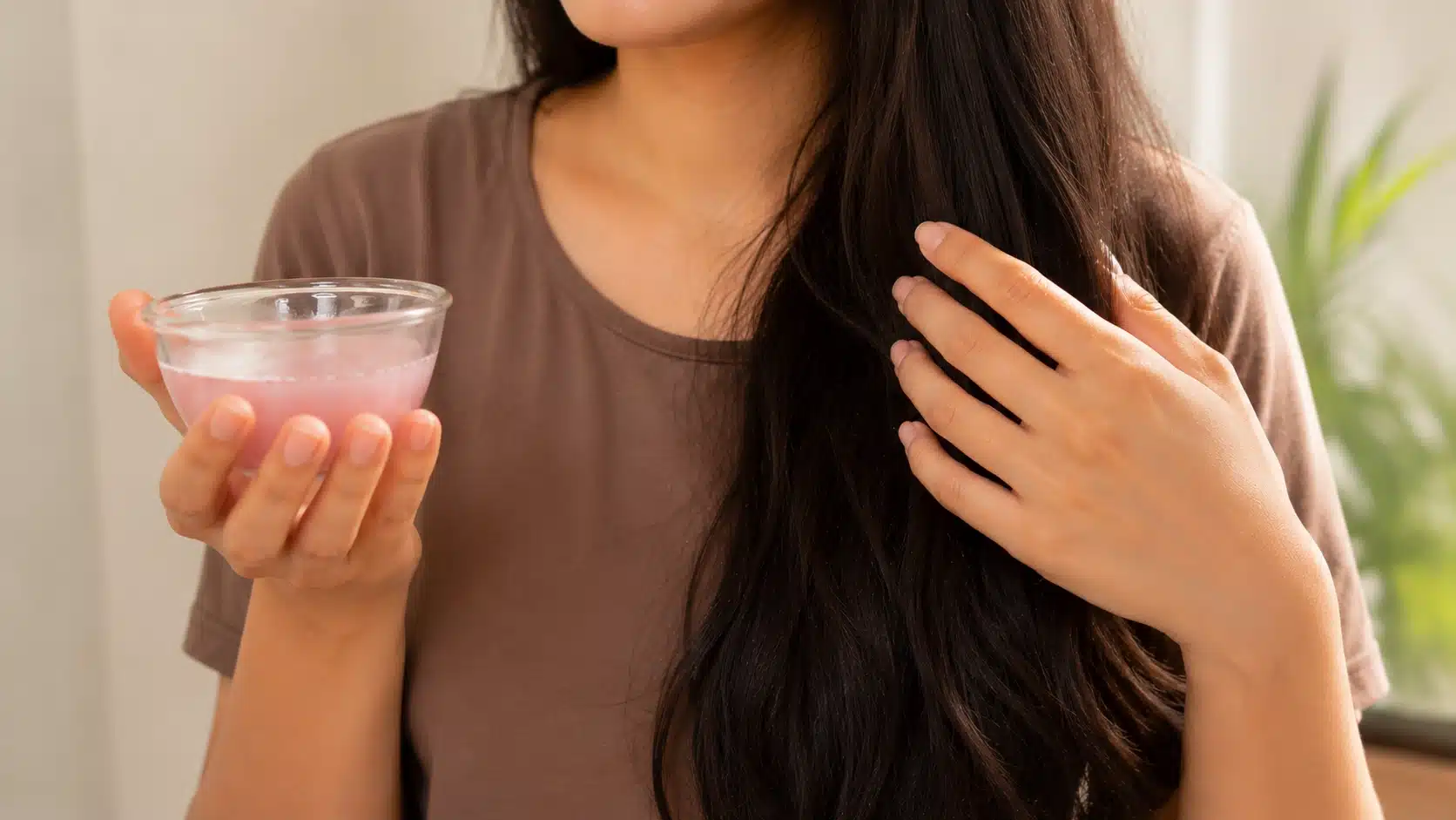 woman holding a small glass bowl of fresh onion juice while showing her healthy hair strands for natural hair care section