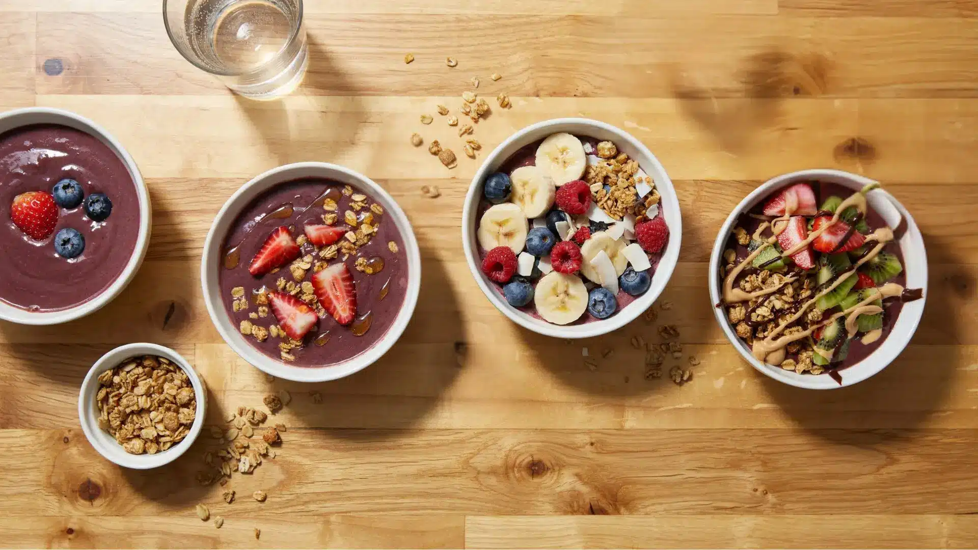 four acai bowls compared side by side from plain to fully loaded with toppings