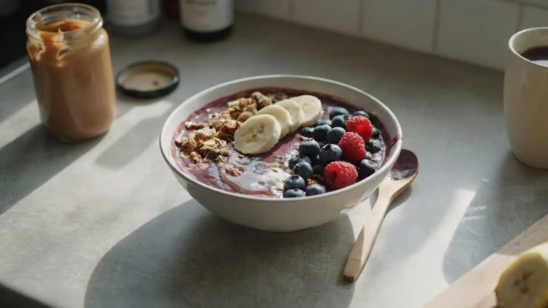 acai bowl topped with banana blueberries raspberries and granola with peanut butter jar
