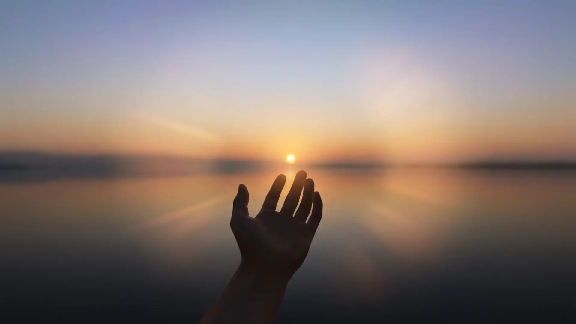 silhouette of an open hand reaching toward a rising sun over a calm, reflective water horizon, symbolizing the common challenges faced during spiritual awakening