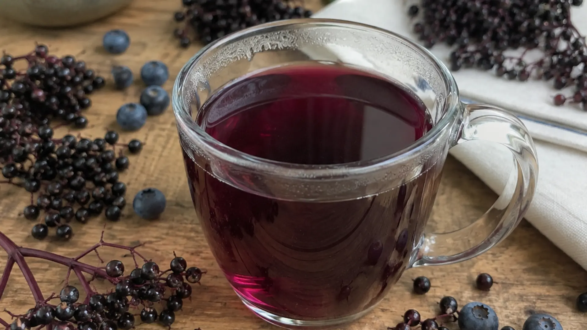 a mug of purple elderberry tea surrounded by fresh elderberries and blueberries