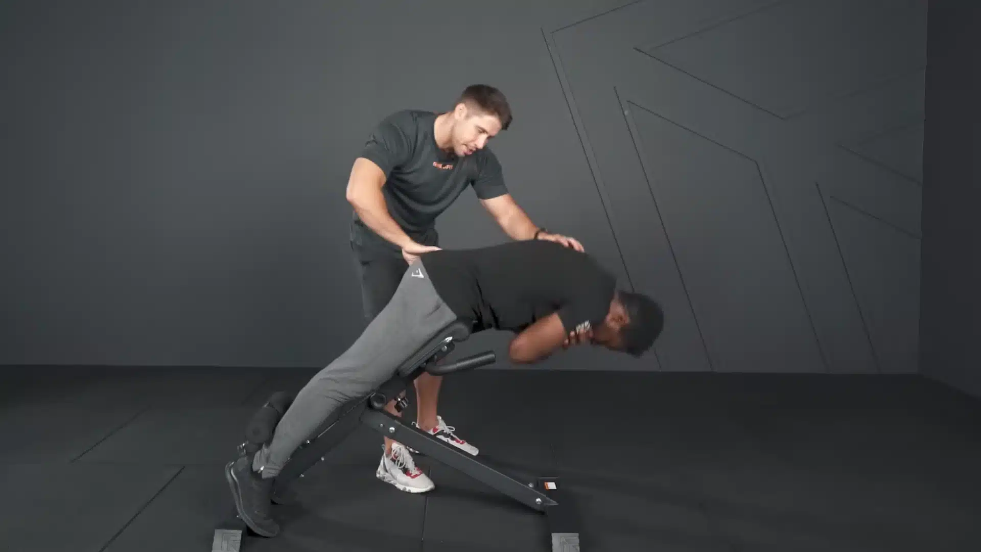 trainer checks an athlete's rounded torso during a glute-focused hyperextension on a roman chair