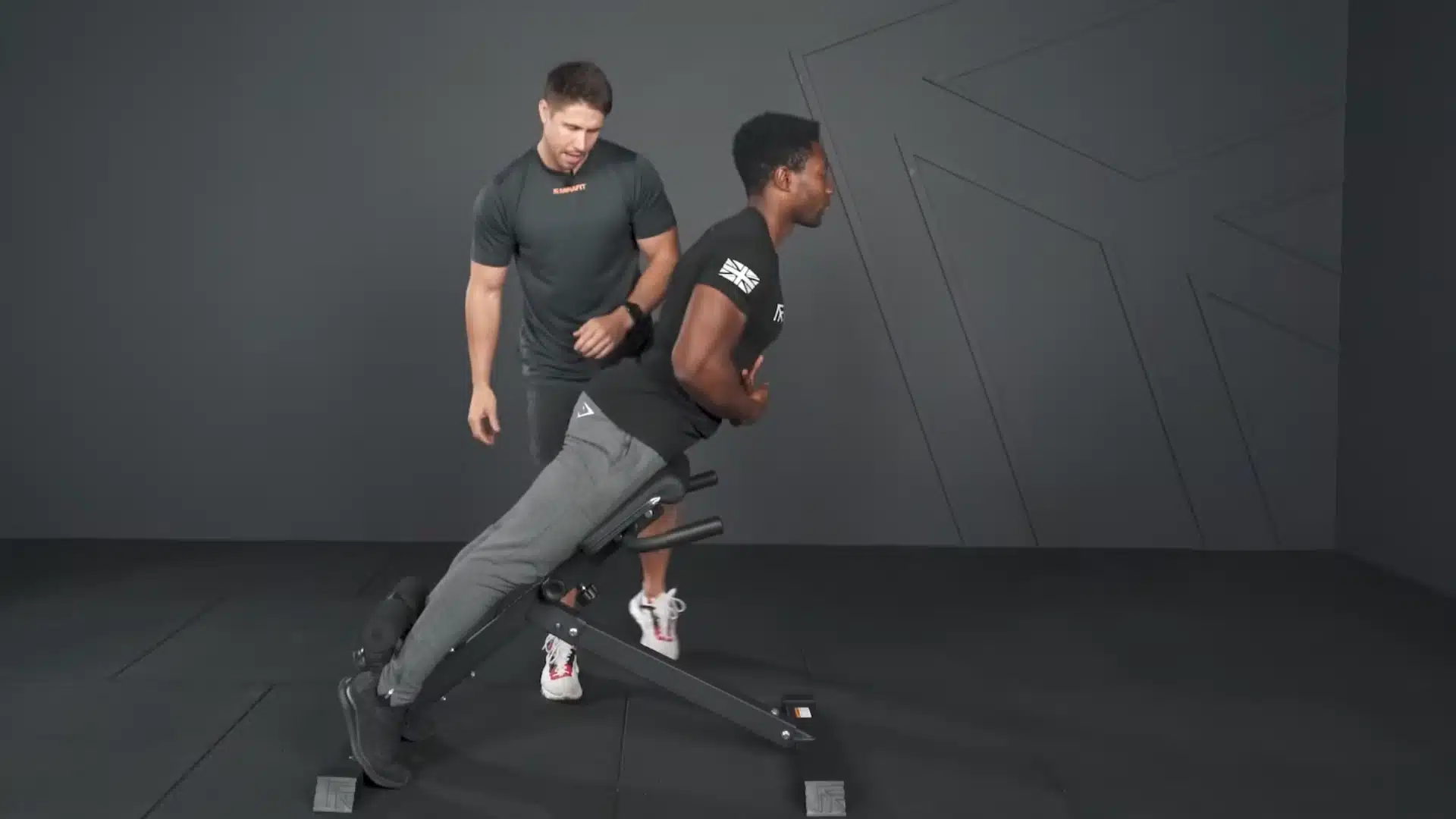 athlete reaches the top of a bodyweight hyperextension as a trainer observes his spinal position