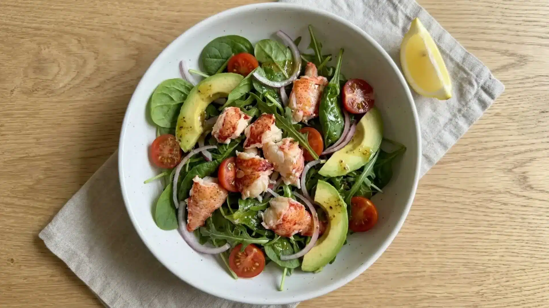 lobster salad with mixed greens, avocado, cherry tomatoes, and red onion in a white bowl