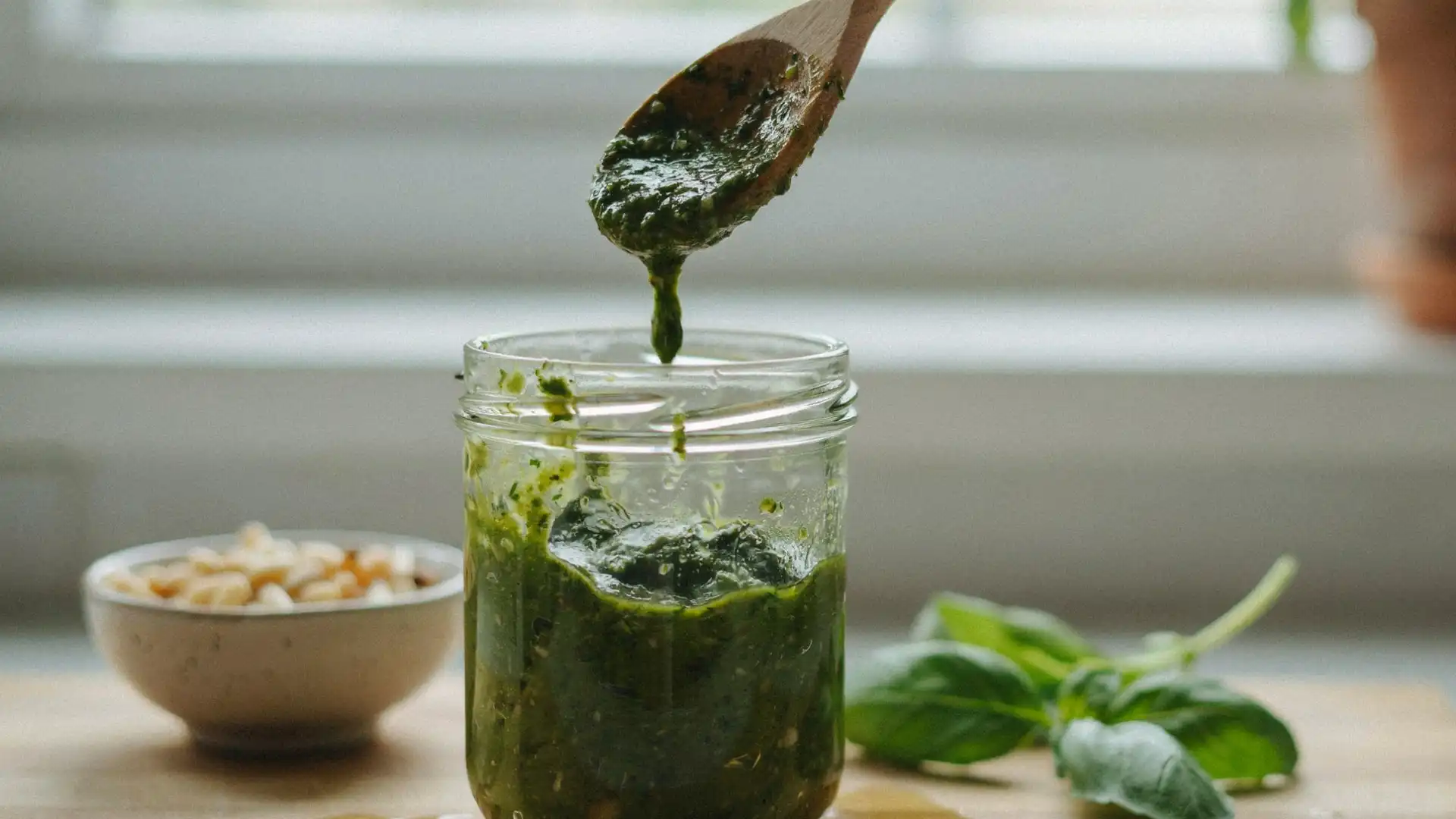 wooden spoon lifting fresh basil pesto from a glass jar