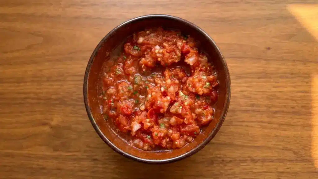 overhead view of a rustic bowl filled with chunky tomato salsa on a wooden table