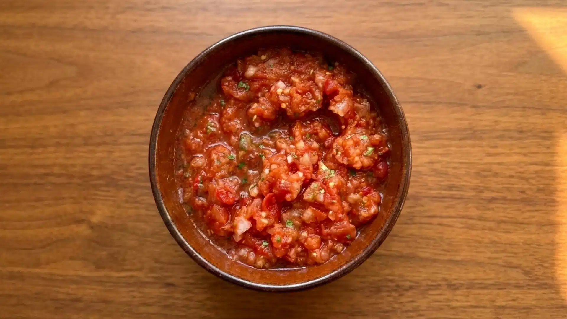 overhead view of a rustic bowl filled with chunky tomato salsa on a wooden table