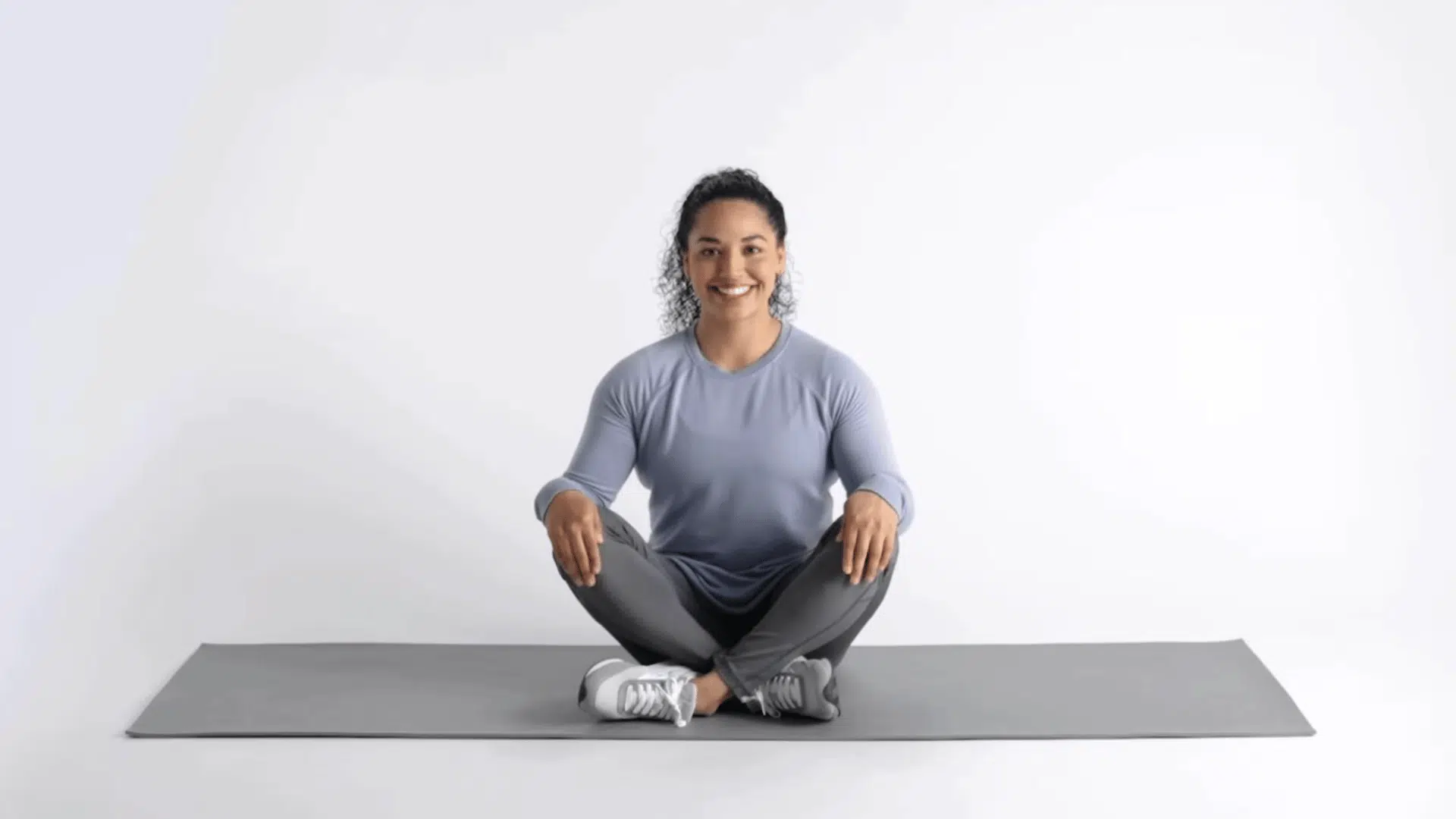 woman sitting cross legged on yoga mat smiling after finishing dead bug exercise
