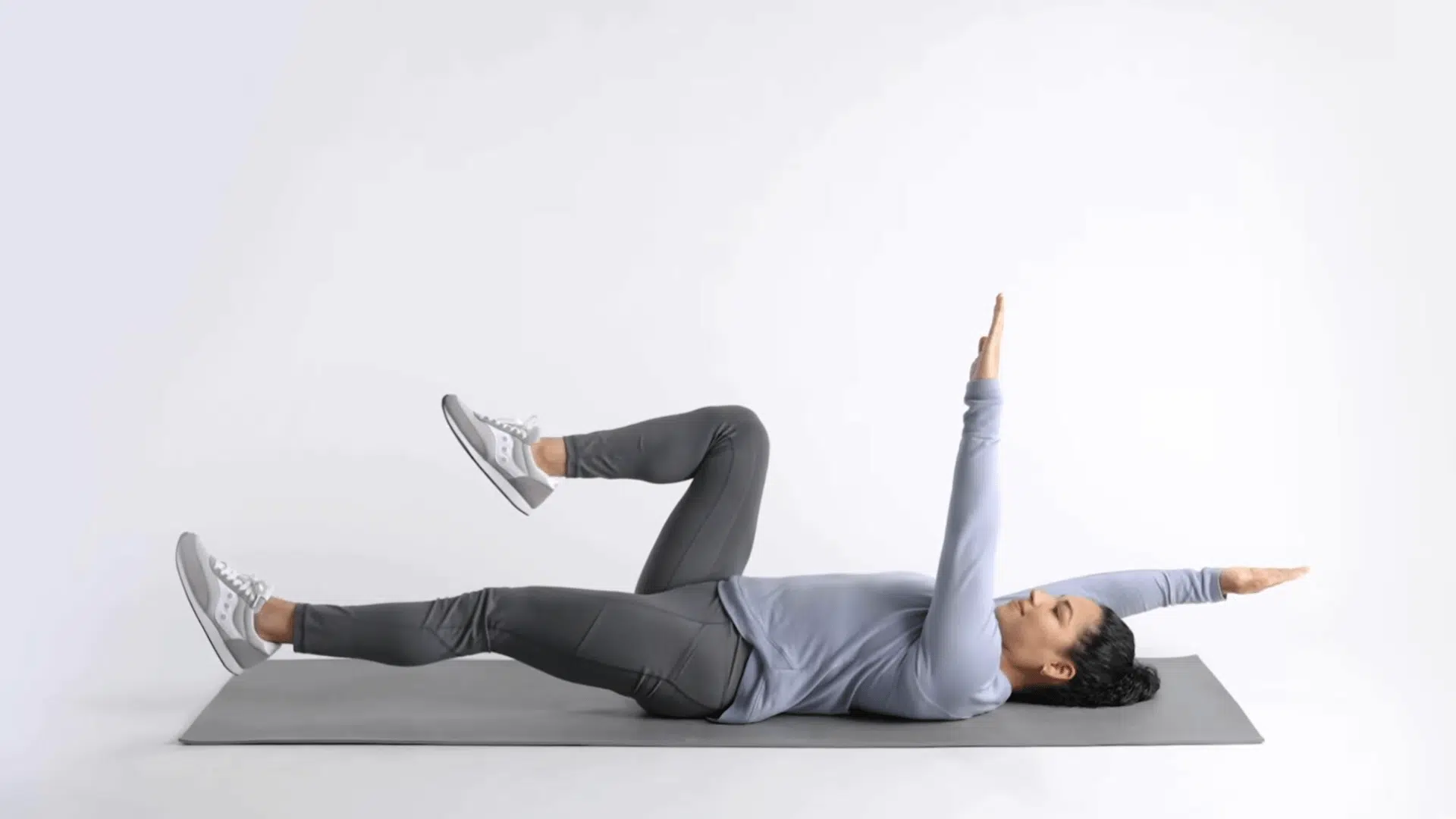 woman on yoga mat extending opposite arm and leg during dead bug exercise movement