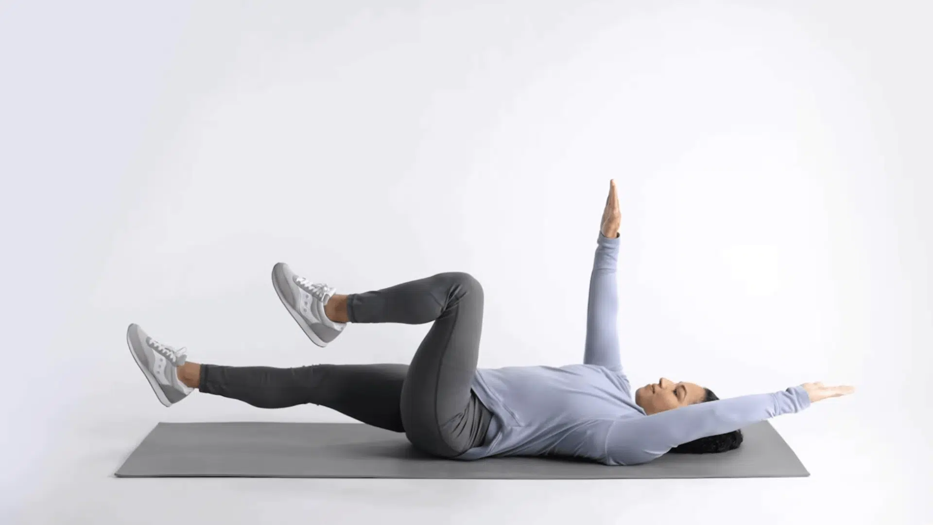 woman on mat extending one arm and opposite leg during dead bug exercise repetition