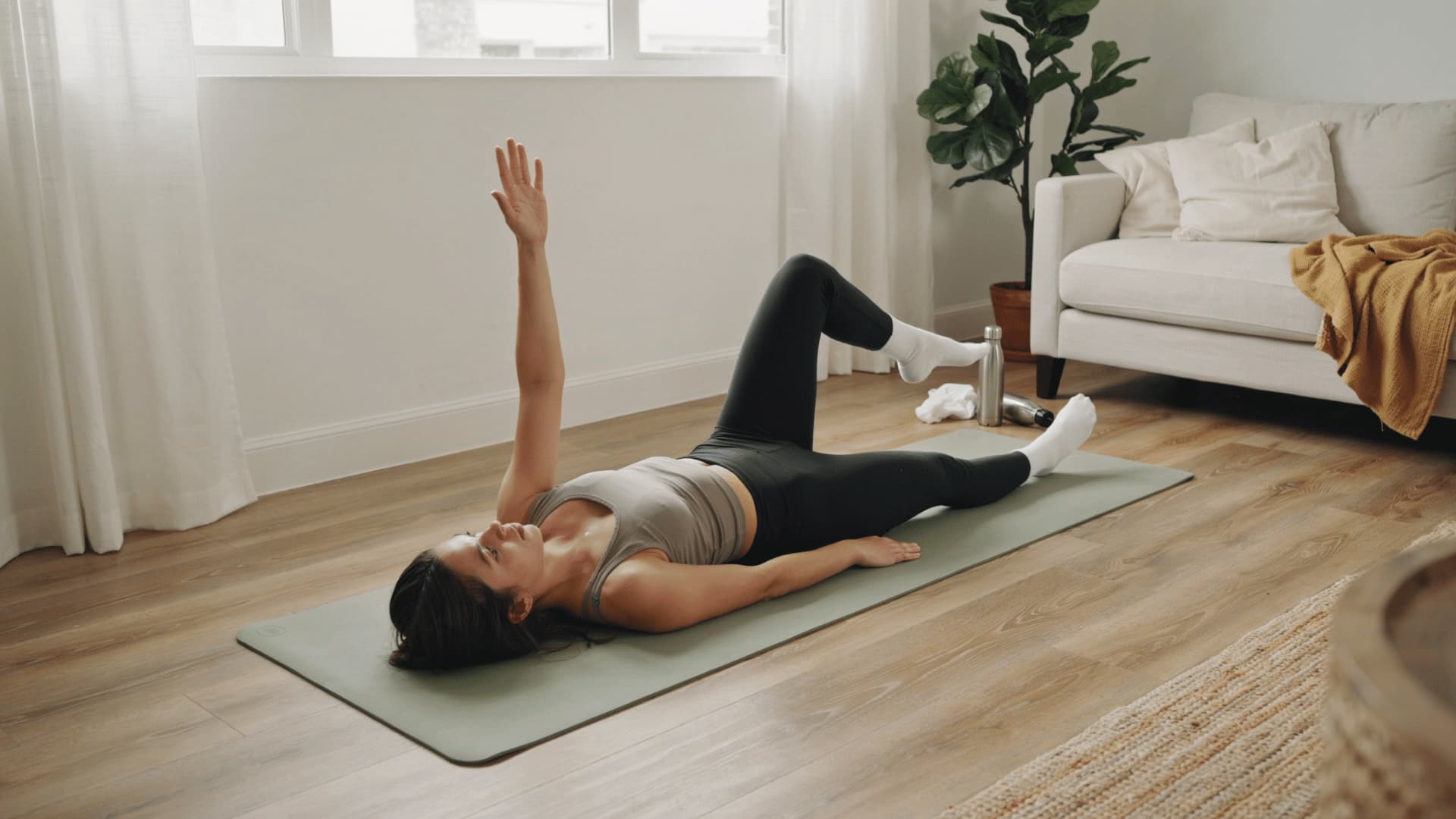 woman performing dead bug exercise on mat with arms raised and one leg extended in living room